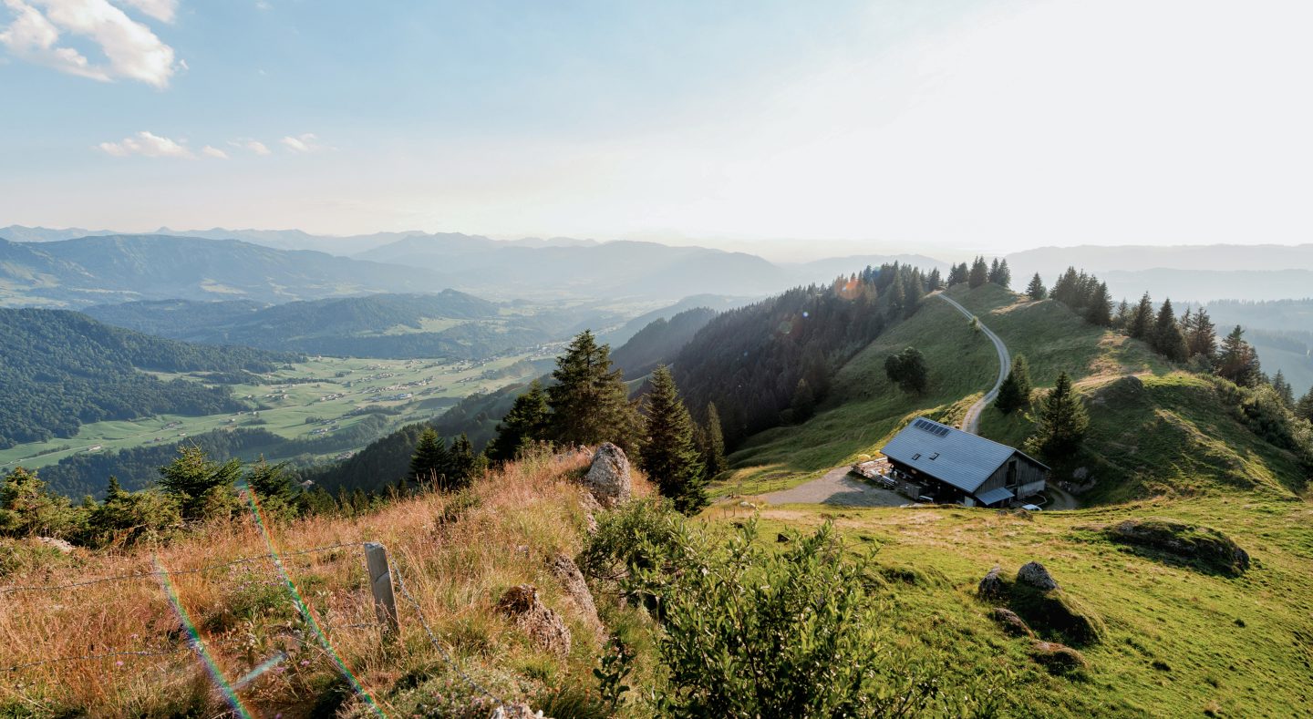 Blick vom Hochhäderich auf 1.565 Metern über eine Alphütte am Bergrücken und weit hinunter ins grüne Tal des Bregenzerwalds.