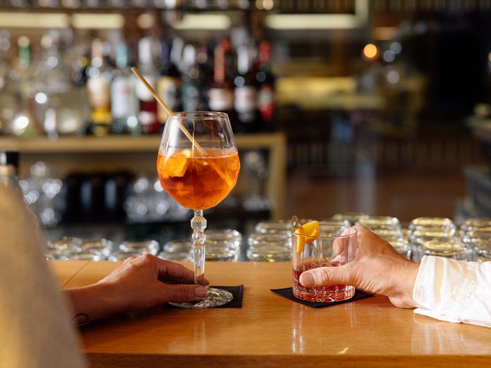 Zwei Hände an der Theke der Wälderbar, eine hält einen Aperol, die andere einen Negroni.