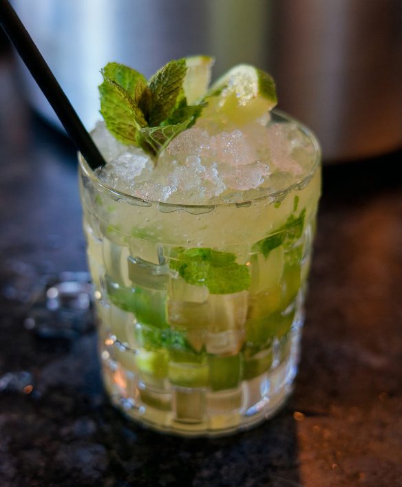 Mojito mit Limettenstücken, frischer Minze und Crushed Ice im geschliffenen Glas auf dem dunklen Tresen der Wälderbar.