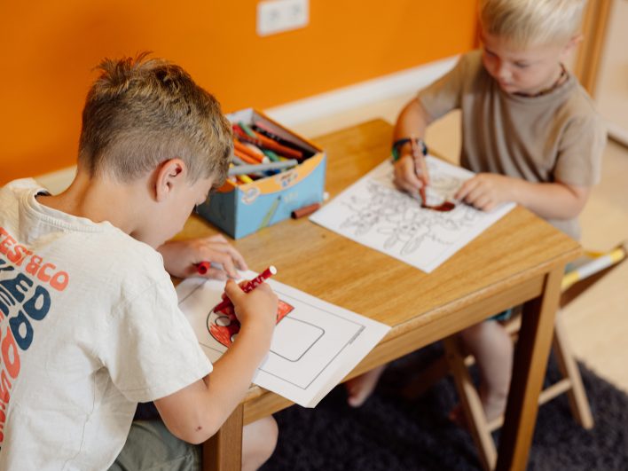 Zwei Jungen malen in der Kinderwelt mit Filzstiften Ausmalbilder an einem kleinen Holztisch.