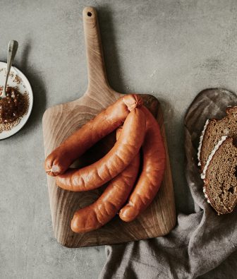 Geräucherte Würste auf einem Holzbrett, daneben Senf und Scheiben dunkles Brot