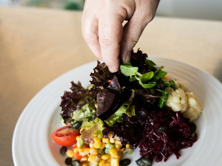 Bunter Salatteller mit Blattsalaten, Feldsalat, Roter Bete, Maissalat, Tomate und Kürbiskernen wird von Hand angerichtet.