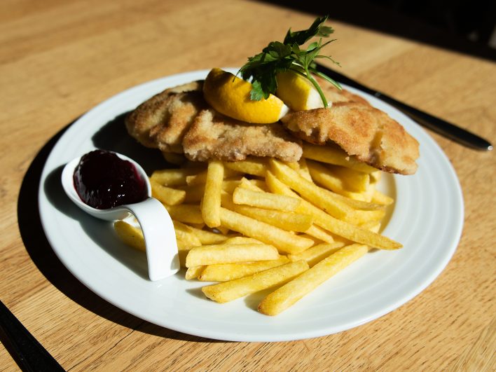 Wiener Schnitzel mit Pommes frites, Zitrone und Preiselbeeren auf weißem Teller im Tagesrestaurant Johann & Frieda.